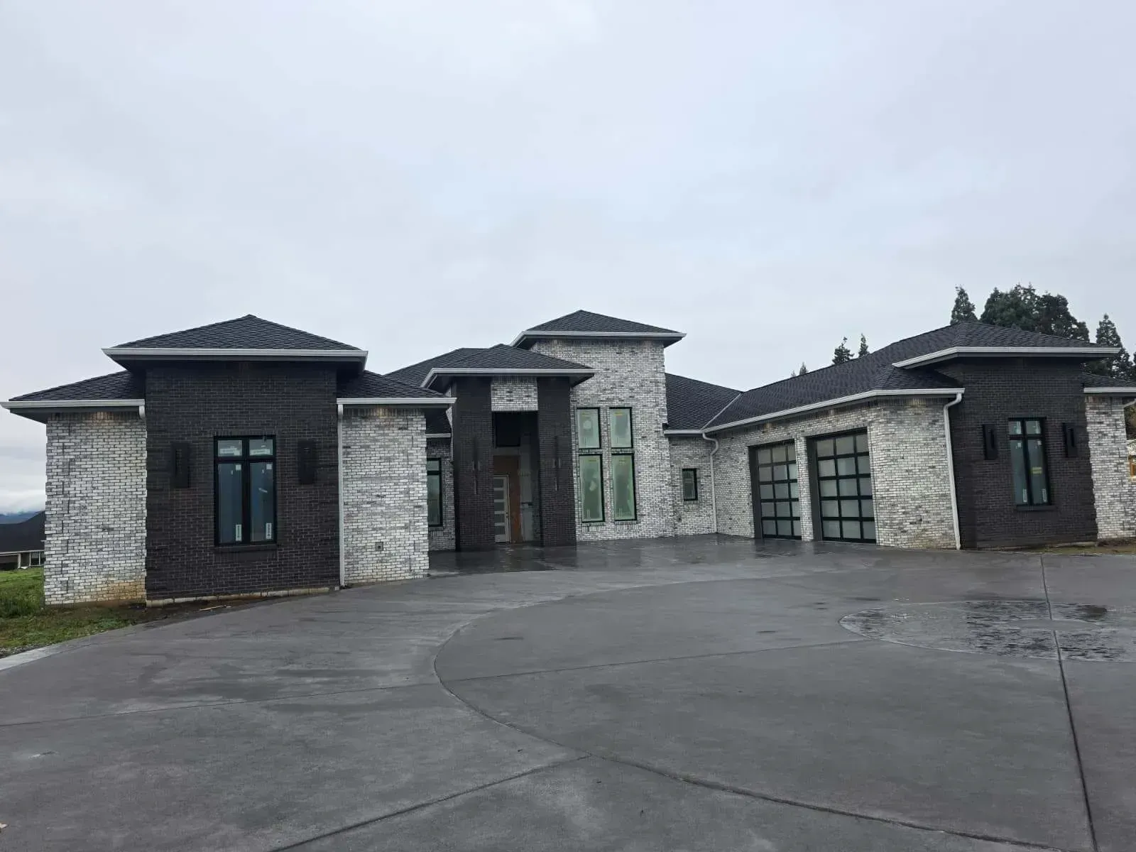 Modern stone house with dark trim and large driveway on an overcast day