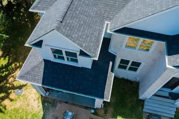 Aerial view of a gray-roofed house with white siding and a dark front porch