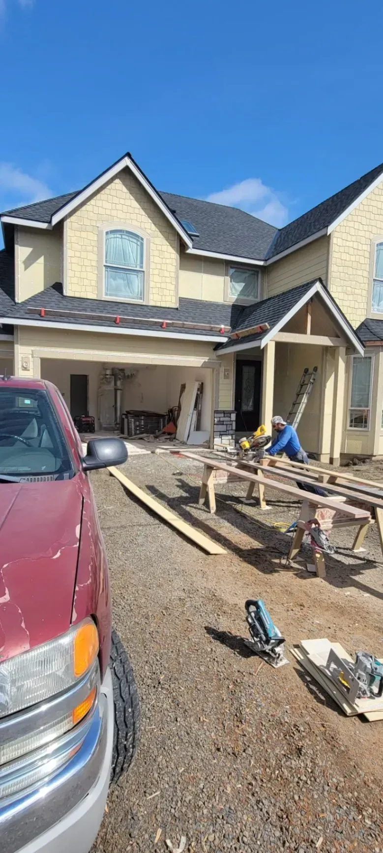 Suburban house under construction with gravel driveway, tools, and a red van in the foreground