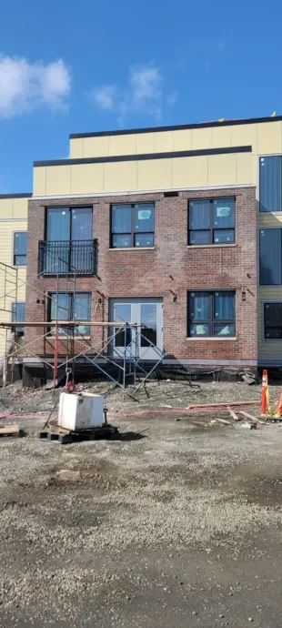 Brick building under construction with scaffold, bare ground, and a blue sky.