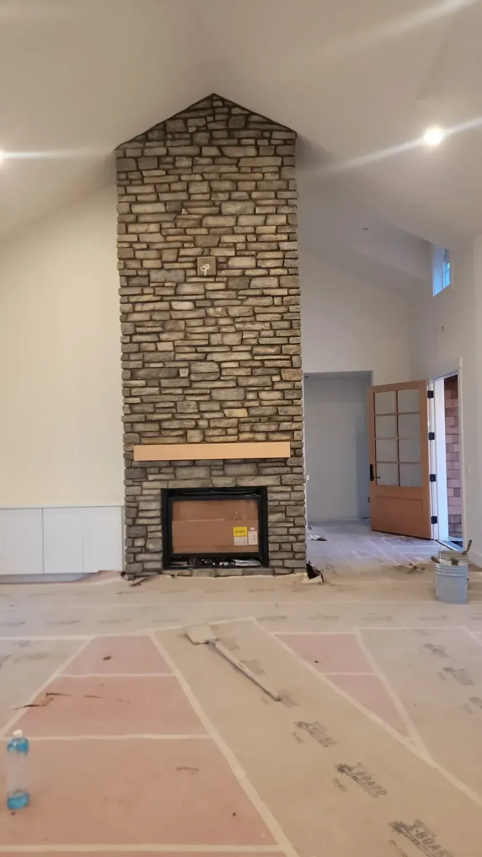 Tall stone fireplace in a mostly empty living room under construction, with unfinished floor coverings.