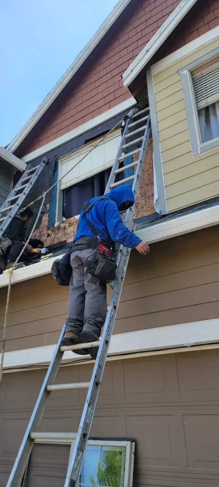 Worker on ladder painting the exterior of a house under the roof eaves.