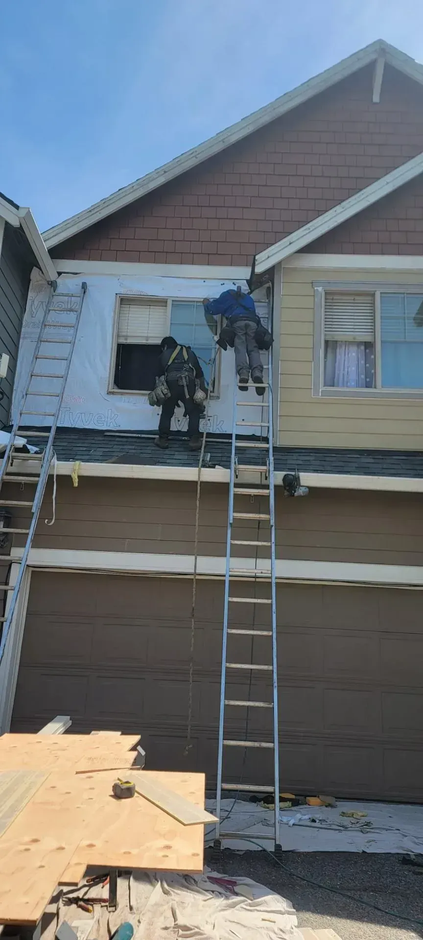 Workers on a ladder repairing siding and roof trim on a house exterior