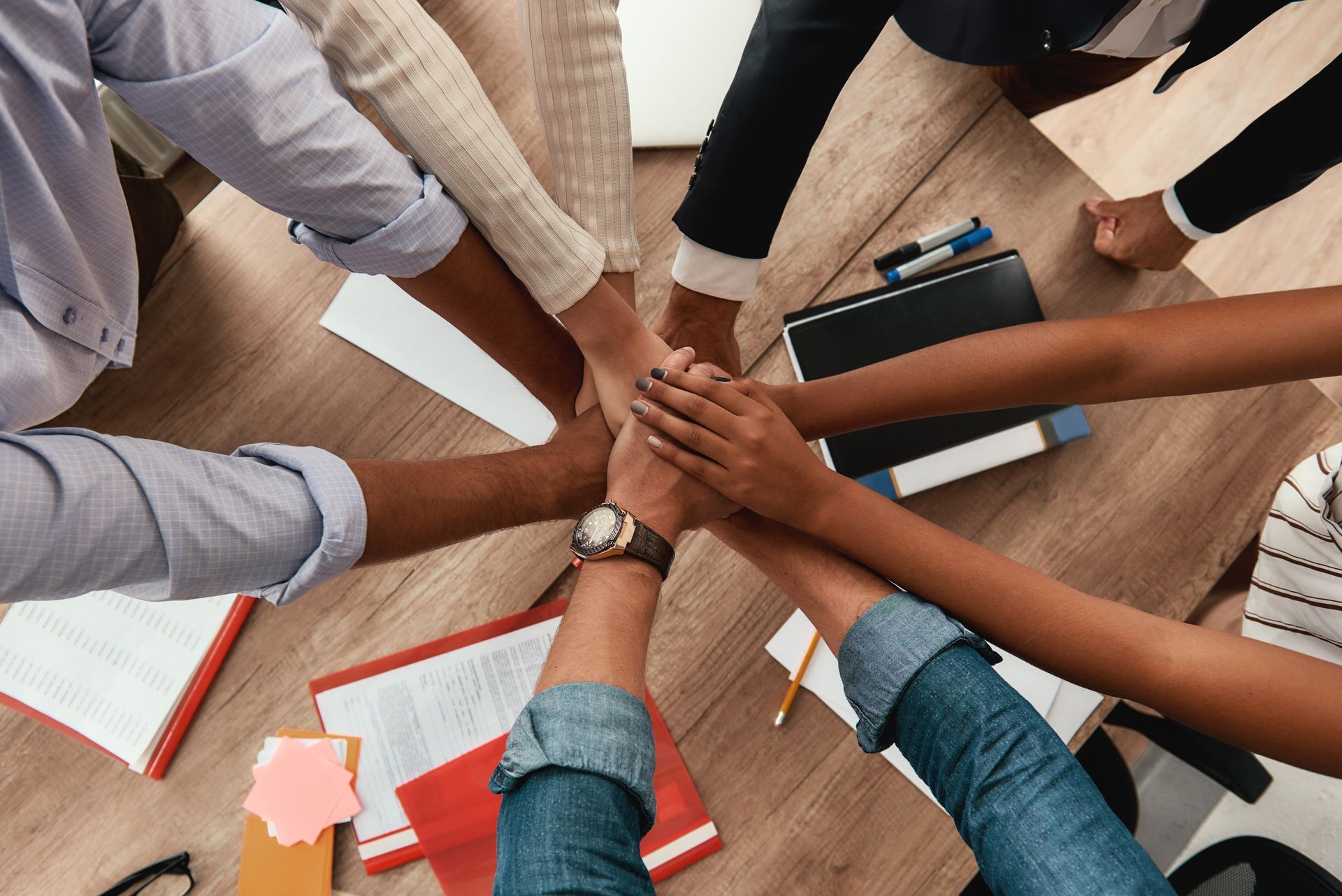 Hands of diverse people in a team huddle, stacked together in unity, on a desk with papers.