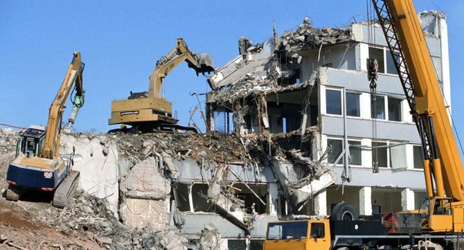Demolition excavators tearing down a partly collapsed building under a clear blue sky