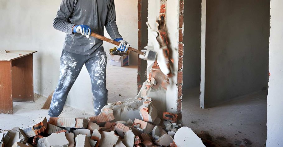 Worker using a jackhammer to break a brick wall in an unfinished room