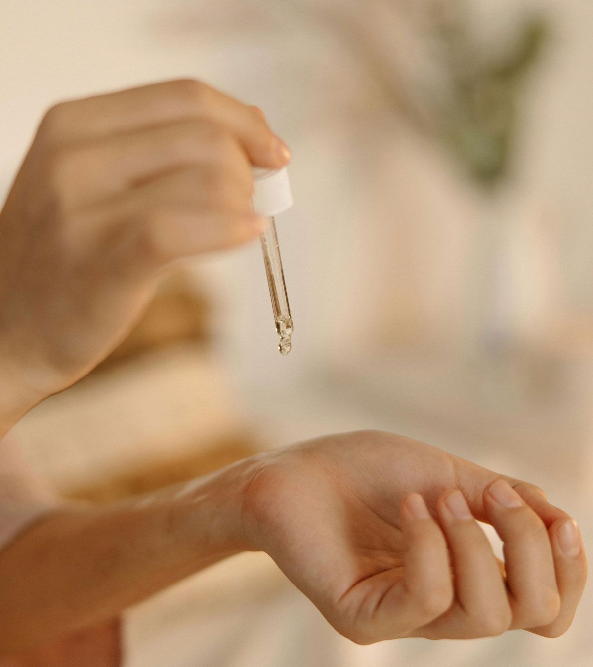 A person is applying a dropper of perfume to their wrist.