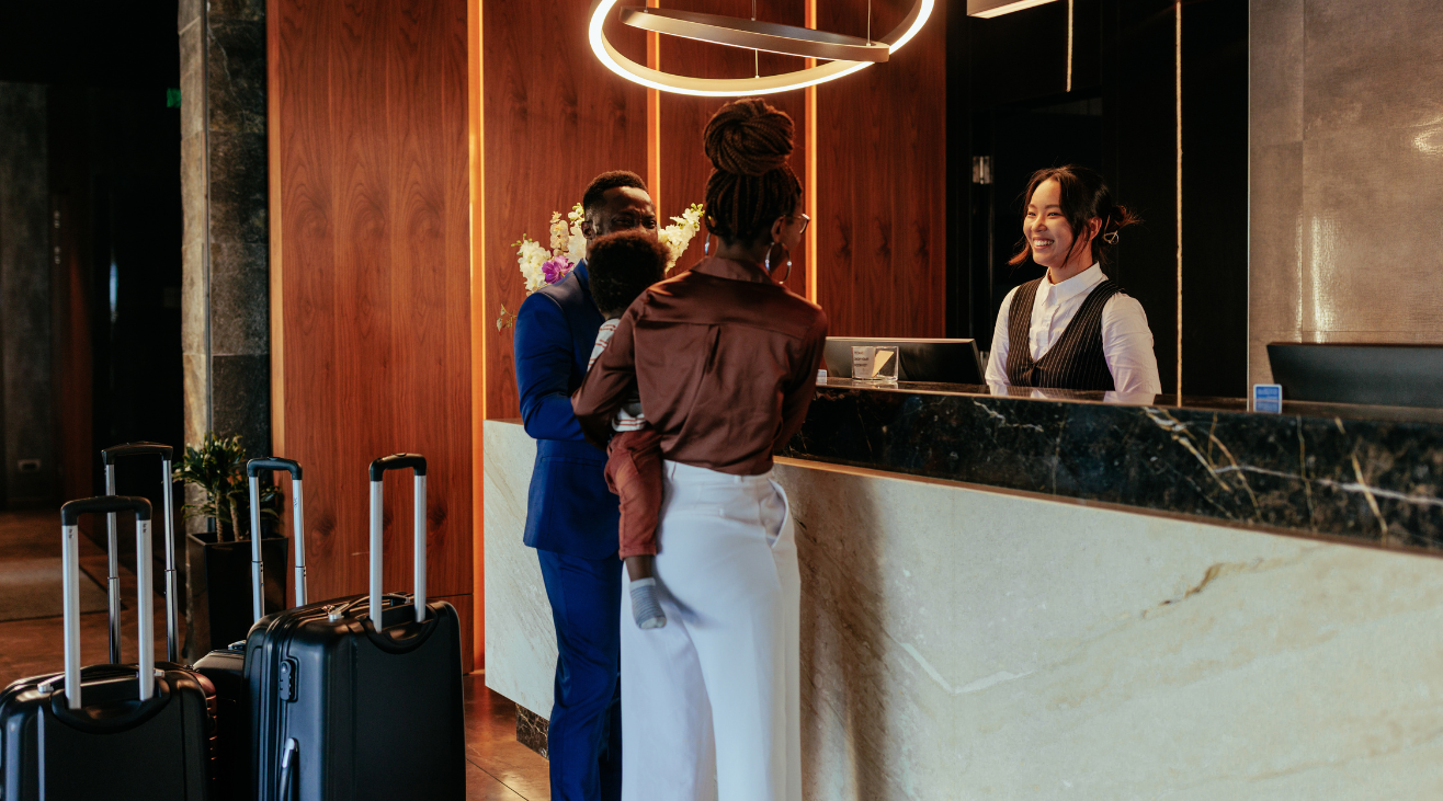 A woman is standing at a hotel reception desk with luggage.