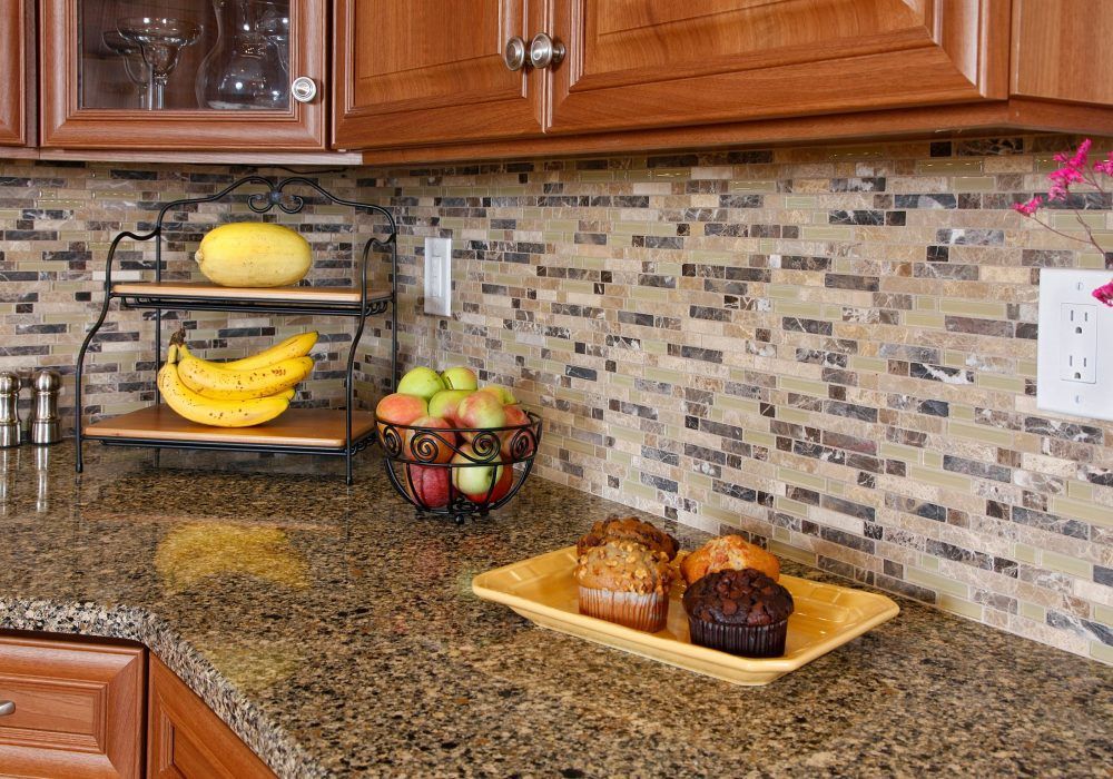 A kitchen counter with a bowl of fruit and muffins on it.
