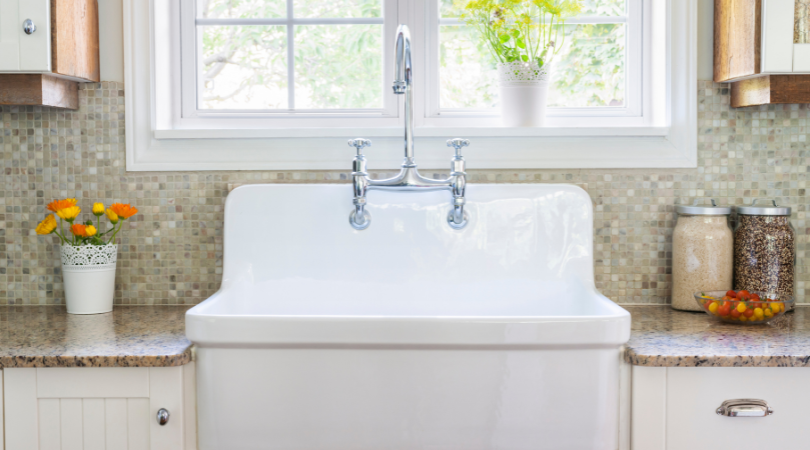 A white farmhouse sink is in a kitchen next to a window.