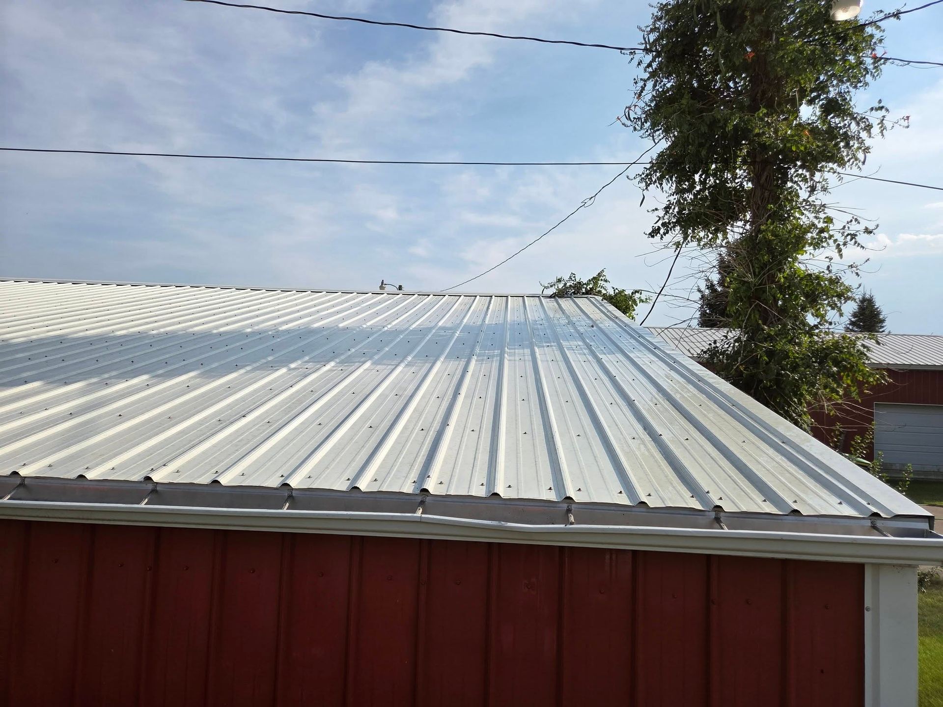Corrugated metal roof with red siding under a blue sky, with a tree and power lines nearby