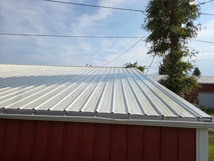Corrugated metal roof with red siding under a blue sky, with a tree and power lines nearby