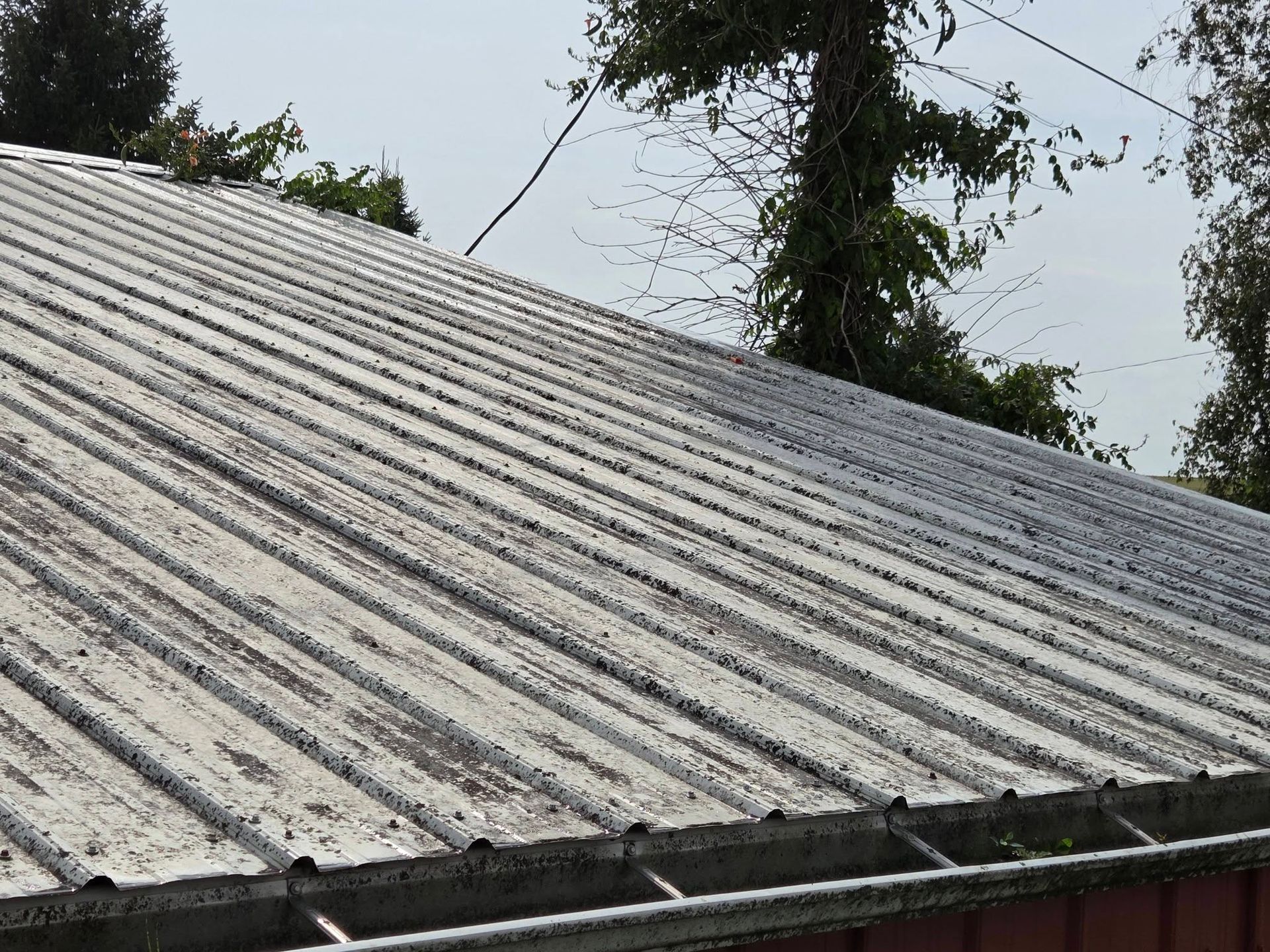 Weathered corrugated roof with dark streaks, viewed at an angle under a cloudy sky.
