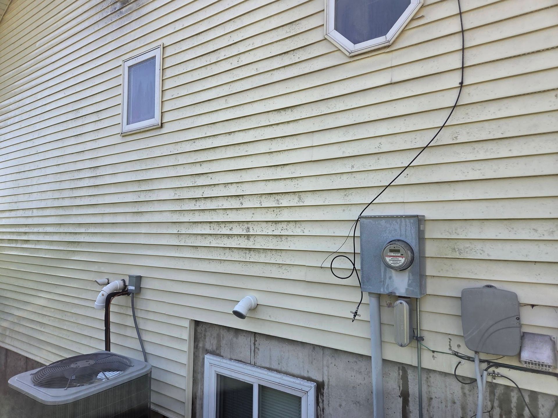 Side of a beige house with an outdoor sink, utility meter, window wells, and cables on the wall.