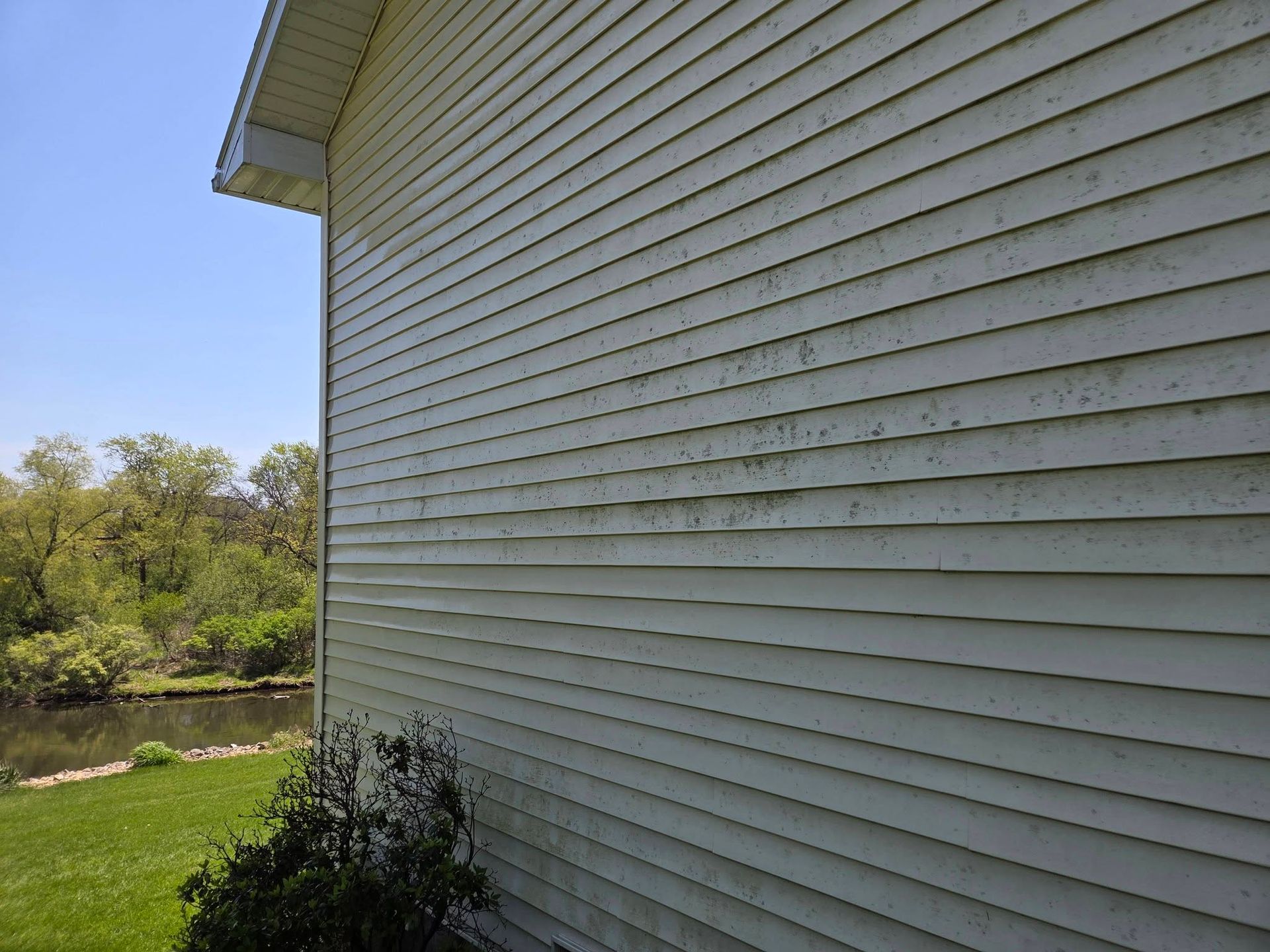 White house siding beside a grassy yard and trees under a clear blue sky