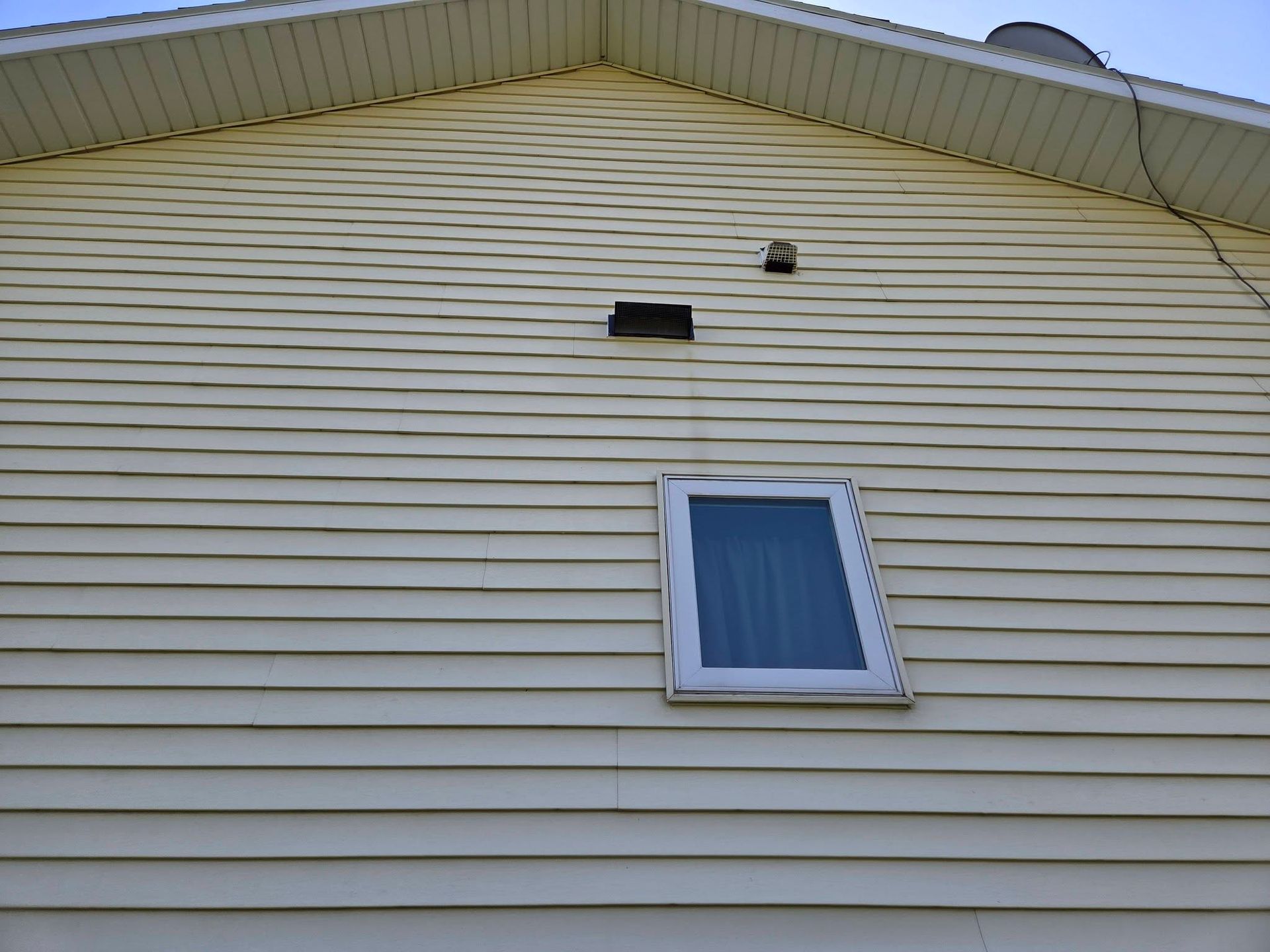 Side of a beige house with vinyl siding, a small window, and roof vents near the gable peak