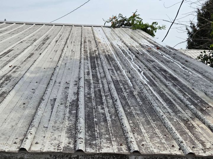 Weathered white corrugated metal roof with dark streaks, viewed from below against a small patch of sky.