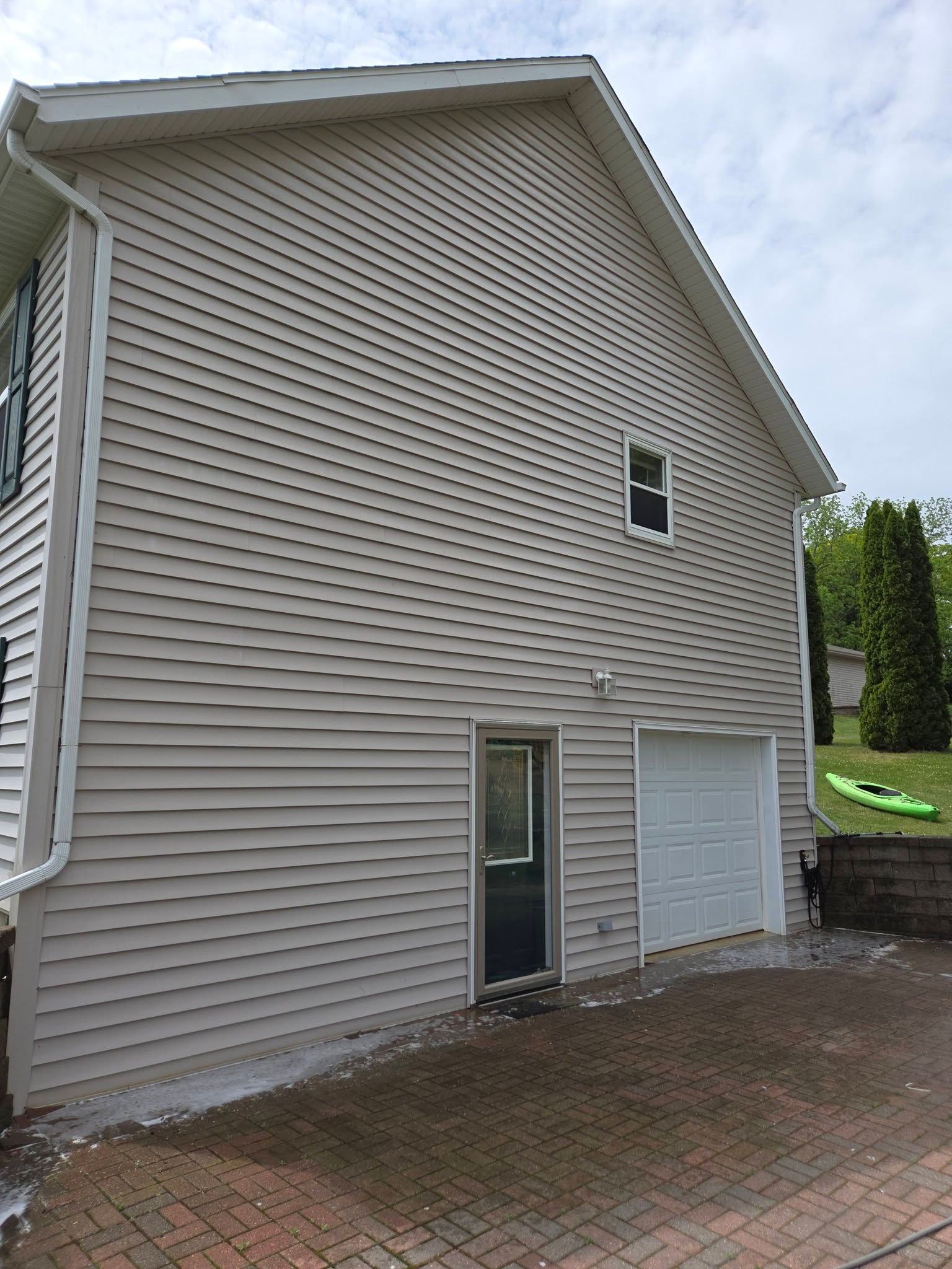 Side view of a beige house with vinyl siding, a small door, garage, and brick driveway.