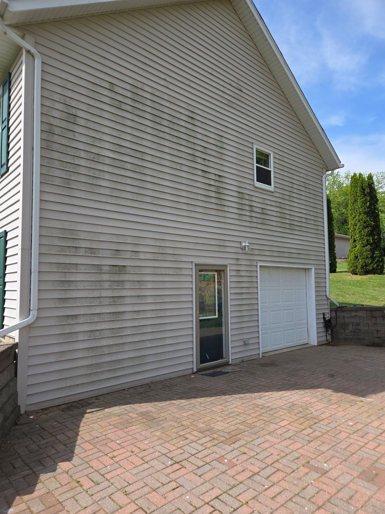 Side view of a gray house exterior with a white garage door, small window, and brick driveway