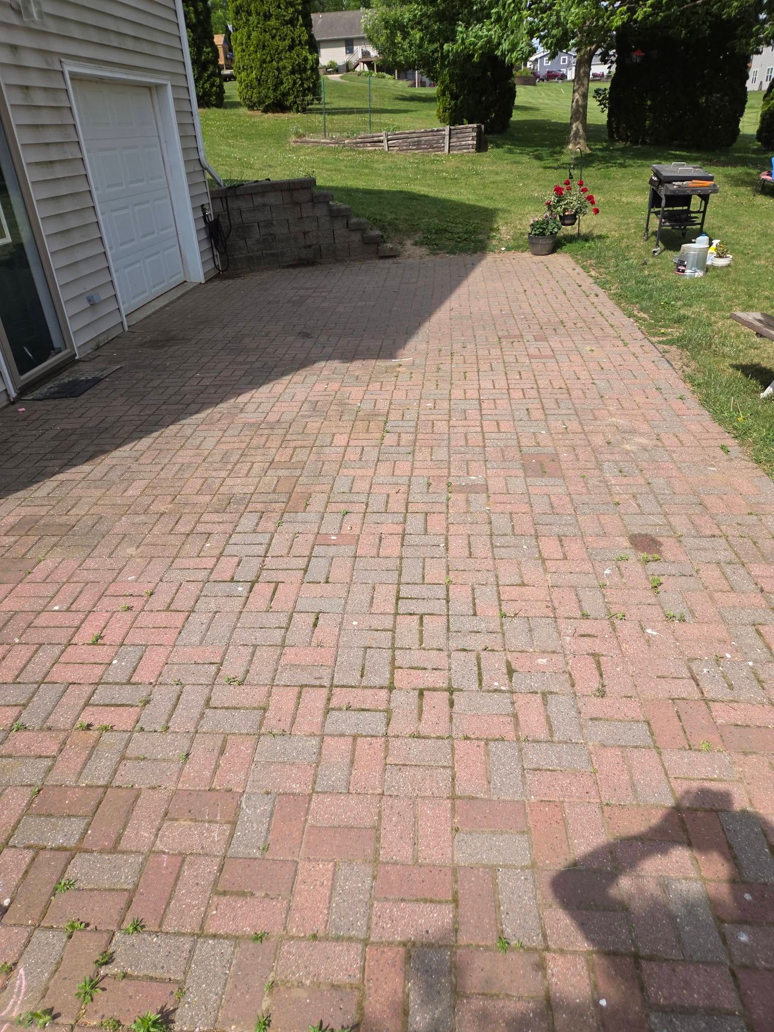 Brick driveway beside a house, with a grassy yard, steps, and a lawn mower in the background.