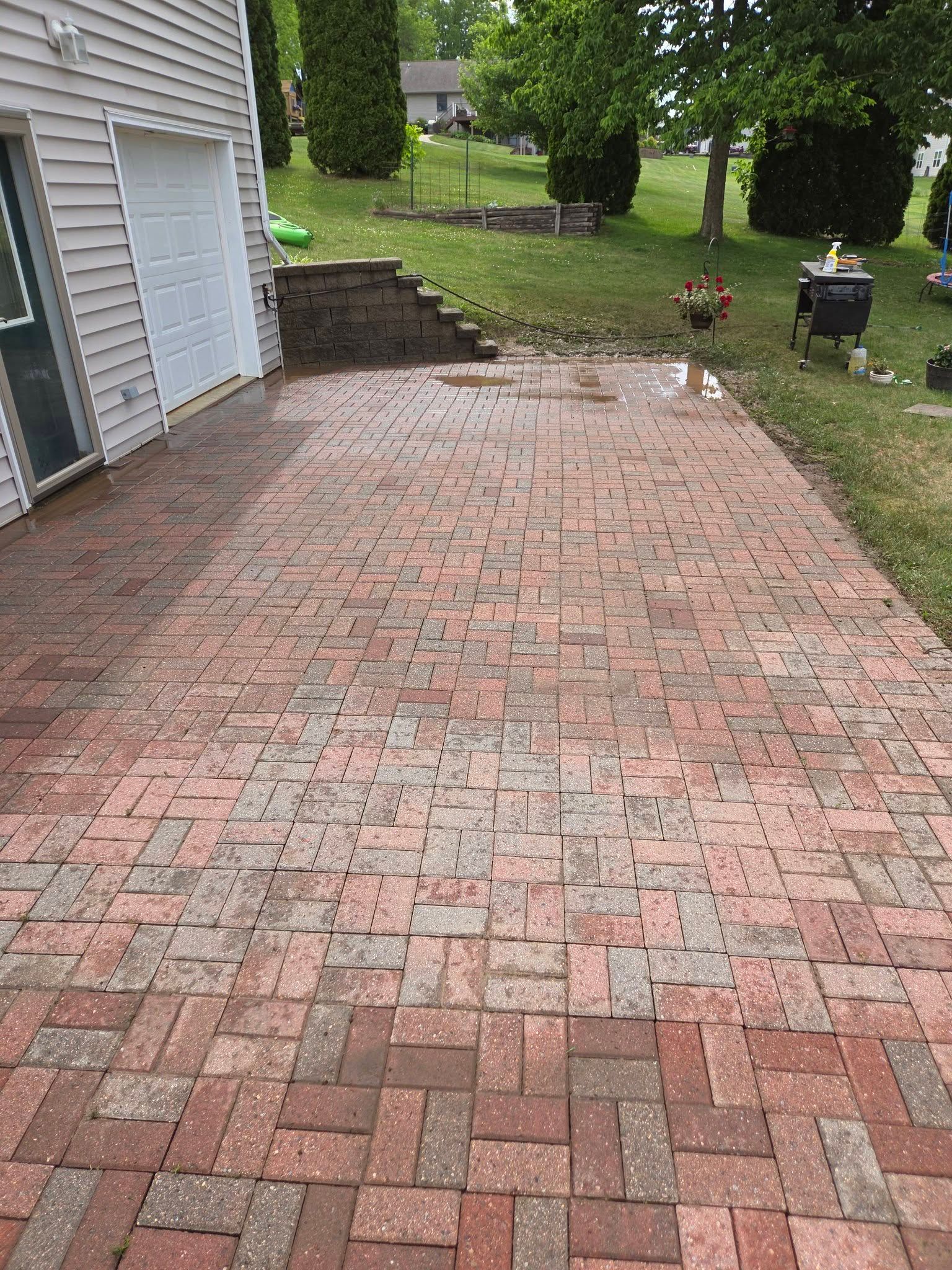 Brick patio beside a house with stone steps leading to a grassy yard and trees
