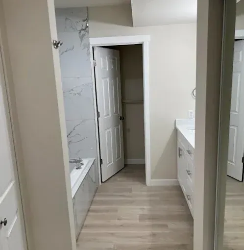 Modern bathroom with marble shower wall, white vanity, and open door to a closet-like space