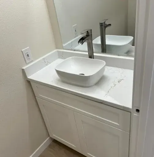 Small bathroom vanity with white countertop, vessel sink, and chrome faucet next to a mirror.