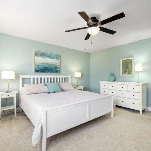 Bright bedroom with white bed, mint walls, ceiling fan, lamps, and white dresser