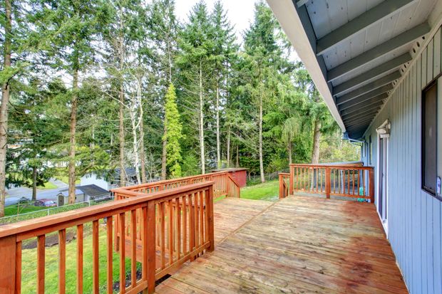 Wooden deck beside a gray house, overlooking tall trees and a green yard