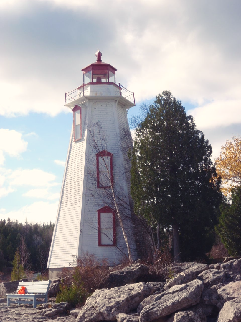 White lighthouse with red trim on rocky shore under a cloudy sky