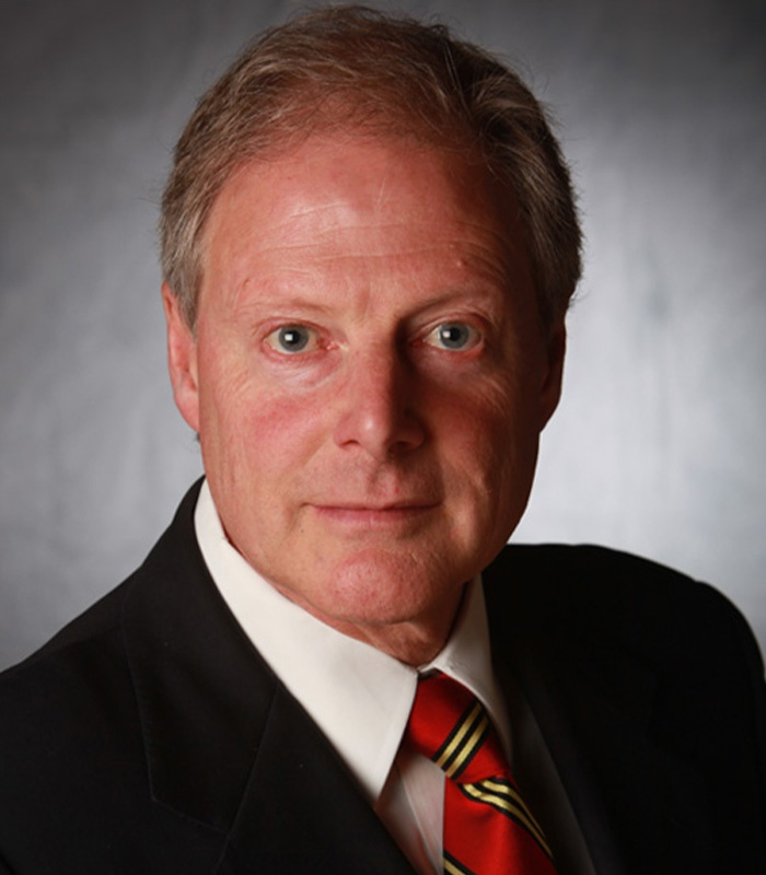 Man in black suit and red tie, looking at the camera.