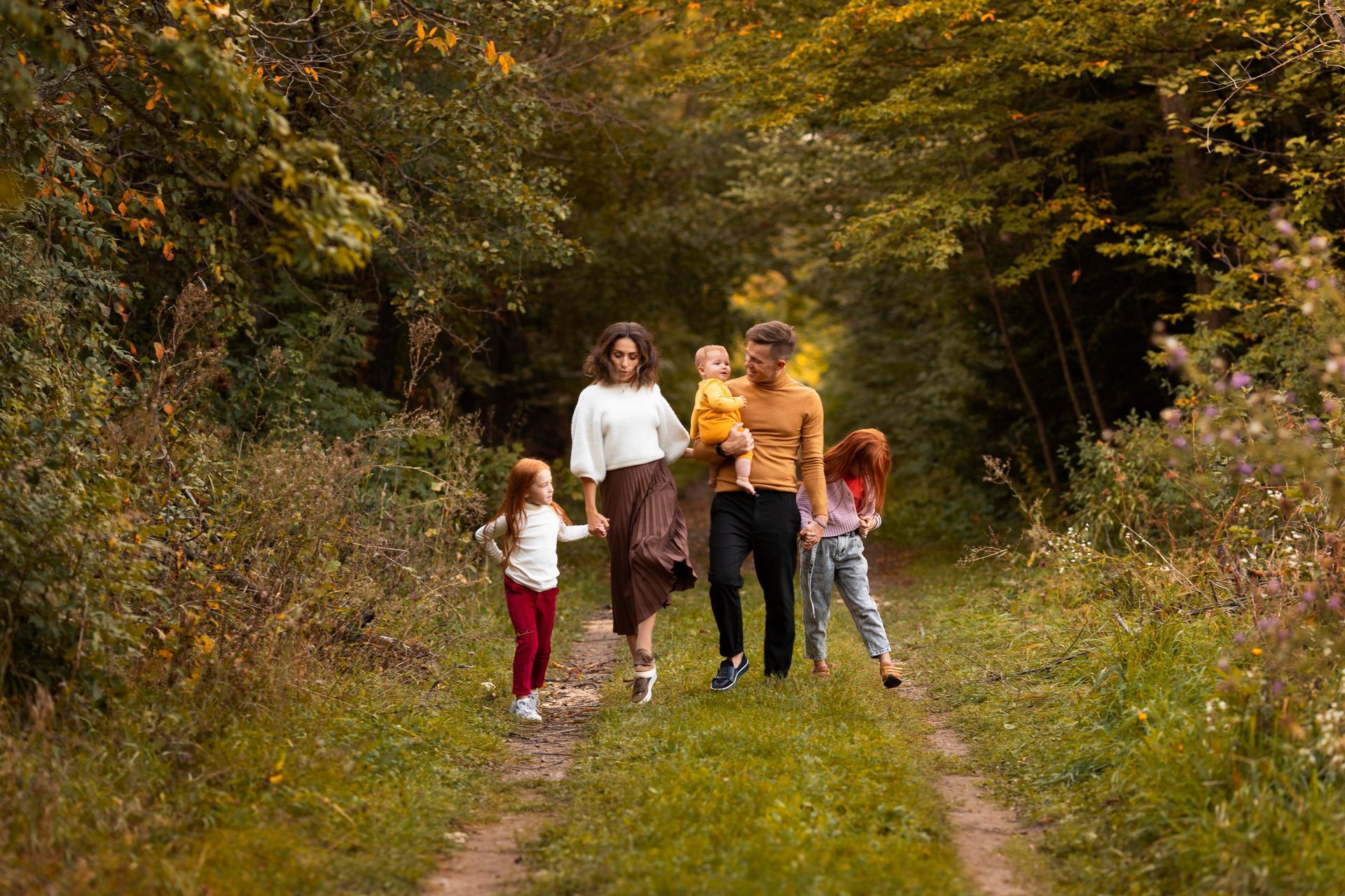 Family walking down a path in a wooded area; two children with red hair, one being carried.