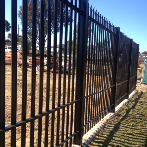 Black metal fence along a dirt path with trees and blue sky in the background