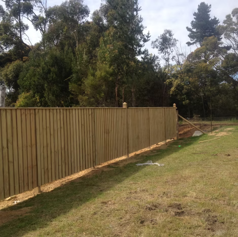 Wooden fence along a grassy yard with trees under a cloudy sky