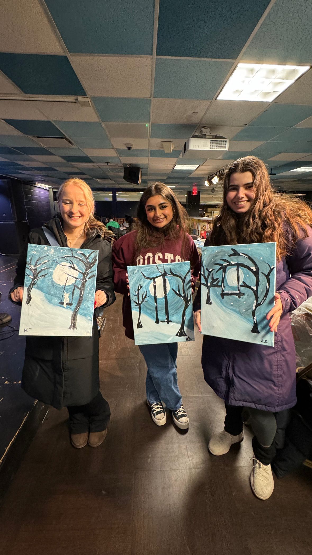 Three women are holding up paintings in a room.