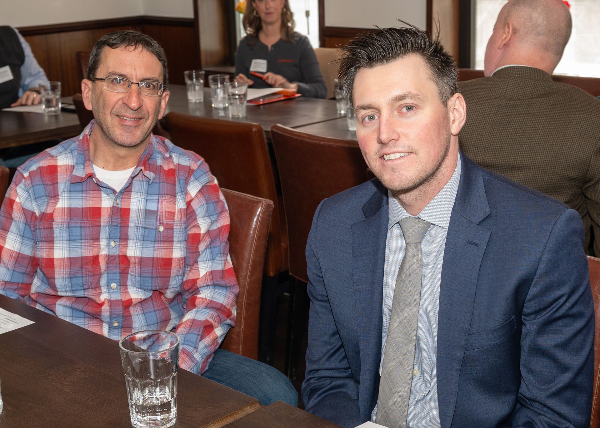 Two men are sitting at a table with glasses of water.