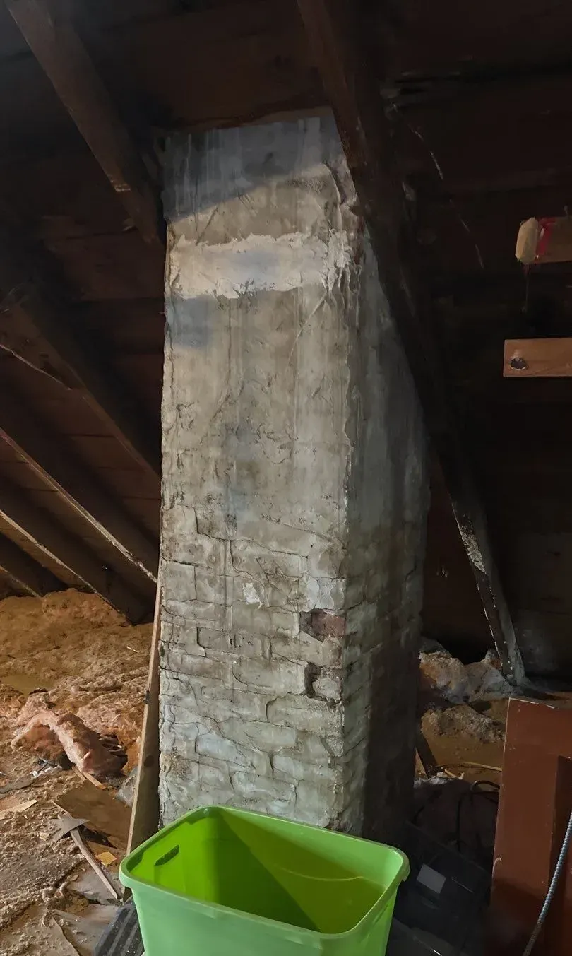 A green bin is sitting next to a brick chimney in an attic.