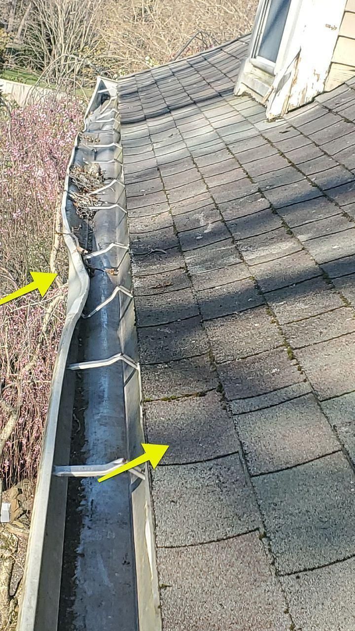 A close up of a gutter on a roof with yellow arrows pointing to it.