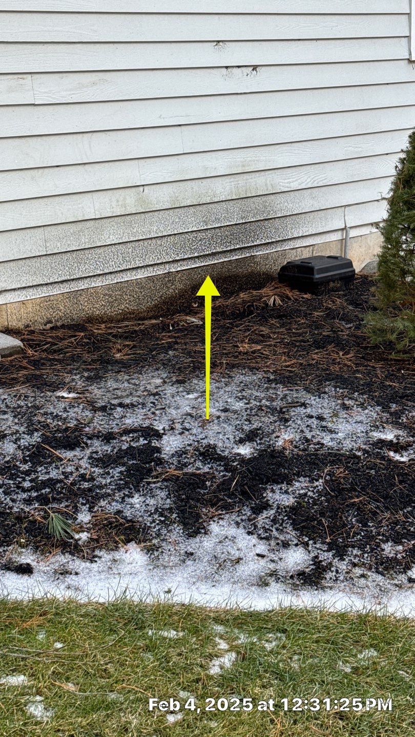 A garden bed in front of a building with mulch, some snow, and a yellow arrow pointing upwards.