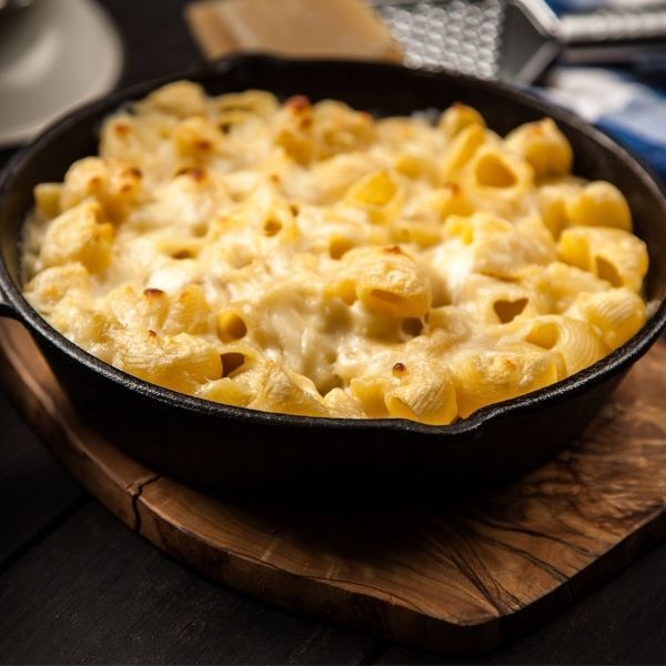 A skillet filled with macaroni and cheese on a wooden cutting board