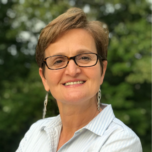 A woman wearing glasses and earrings is smiling for the camera.