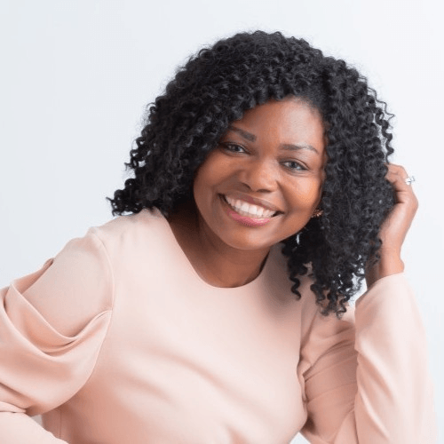 A woman with curly hair is wearing a pink shirt and smiling