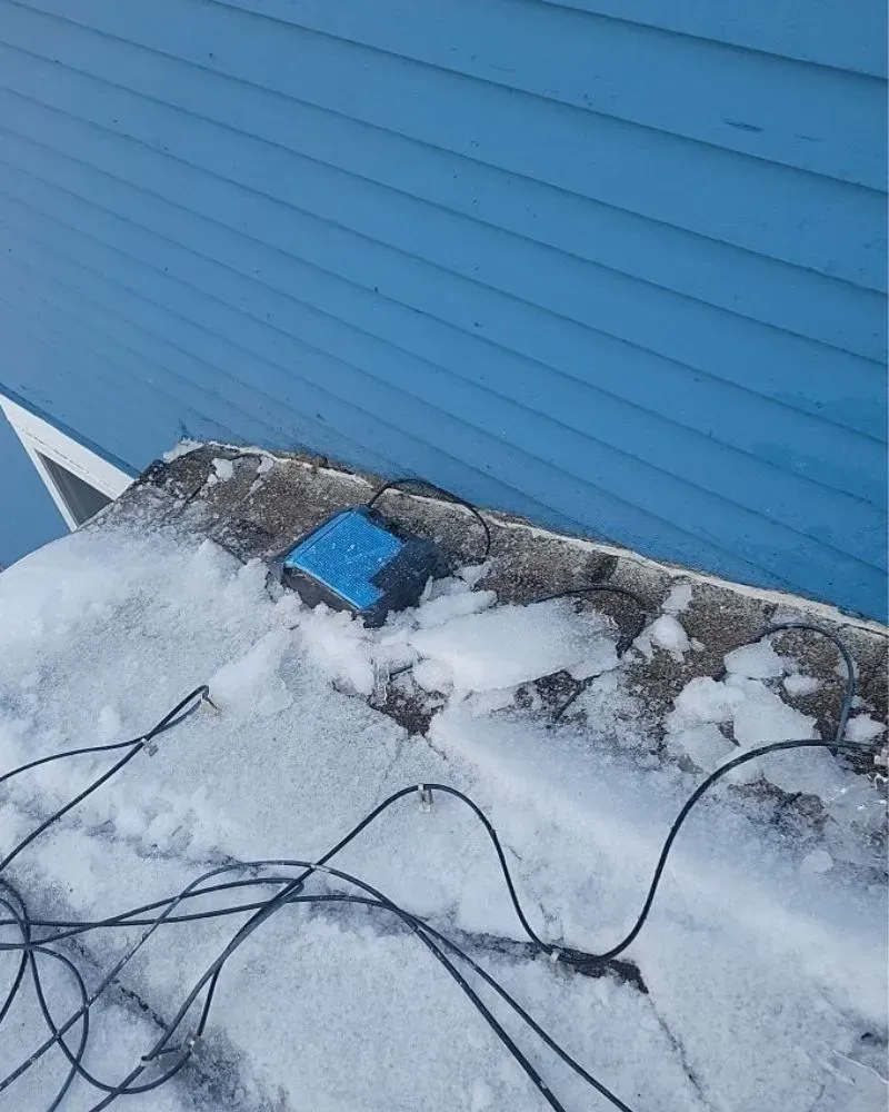 A blue box is sitting in the snow next to a blue building.