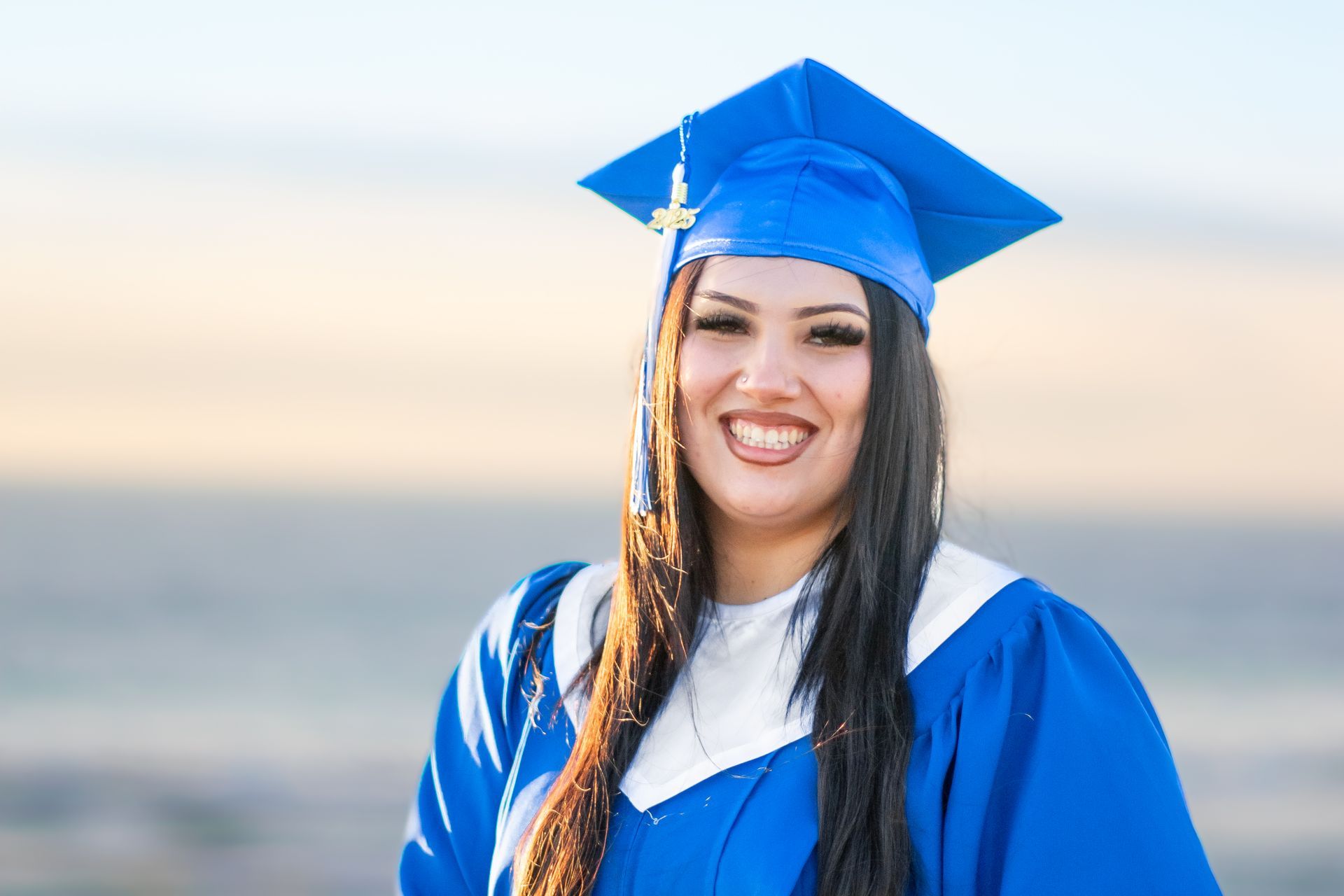A woman is wearing a blue graduation cap and gown and smiling.