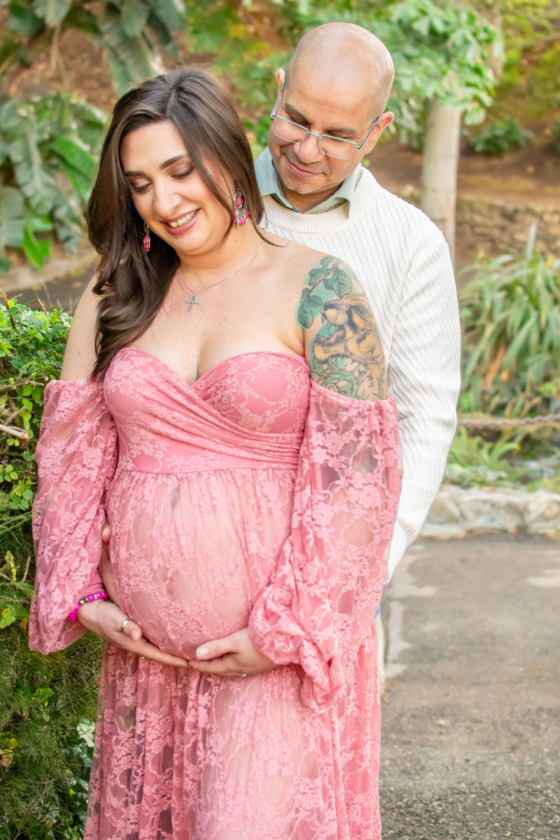 A pregnant woman in a pink lace dress is standing next to a man. Maternity. Couple photo.