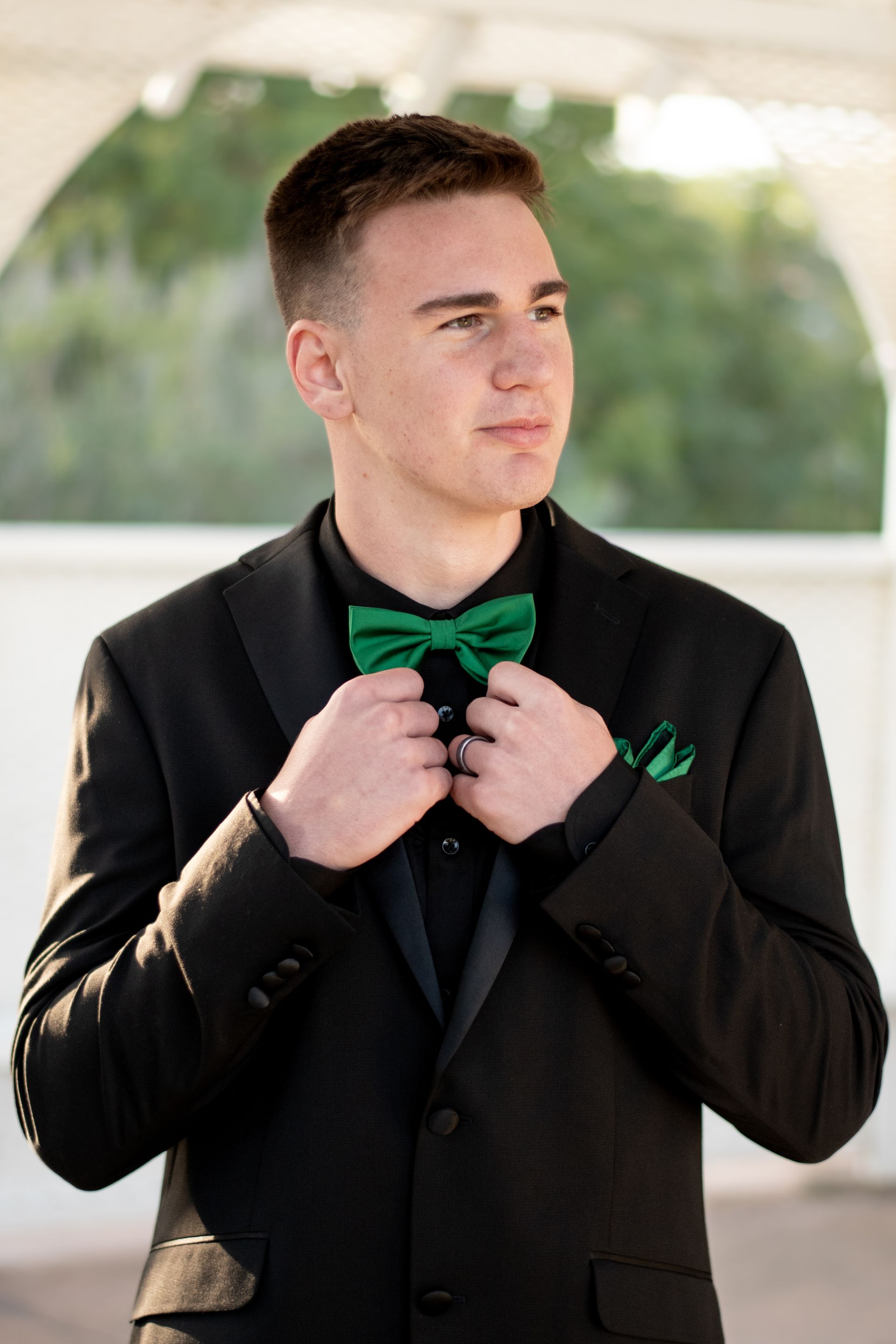 Man in black suit and green bow tie adjusts bow tie, looking off to the side.