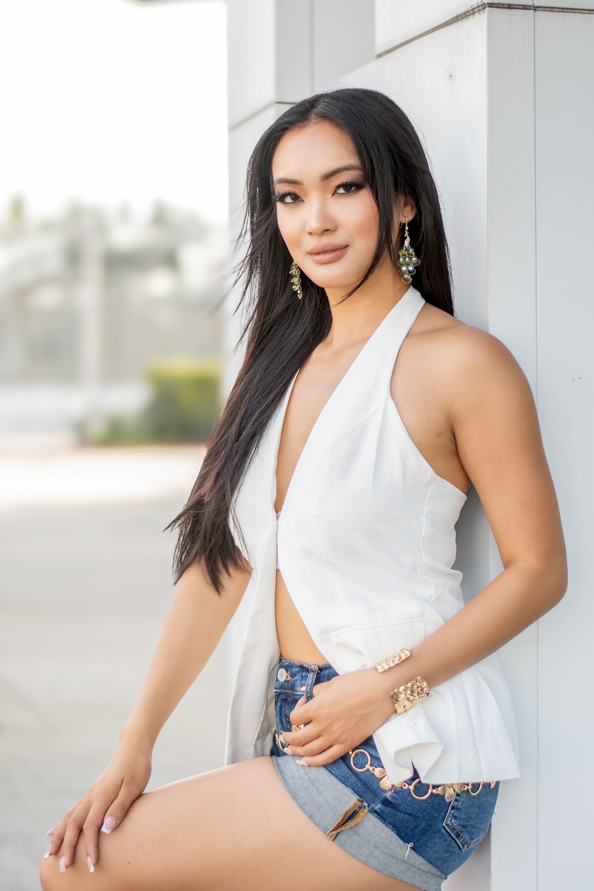 Woman in a white top posing outdoors with one arm raised, looking at the camera.