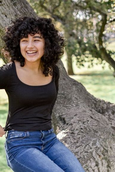 A woman with curly hair is sitting on a tree branch.