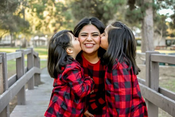 A woman is being kissed on the cheek by two little girls. Banning Park