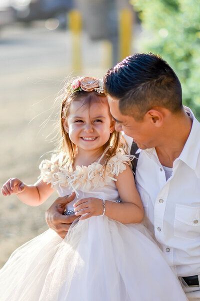 A man is holding a little girl in a white dress at White Point Beach in SoCal